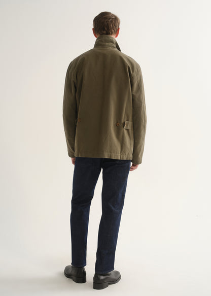 Person wearing dark indigo straight leg jeans with an olive green jacket and black boots, back full body view on a light grey background.
