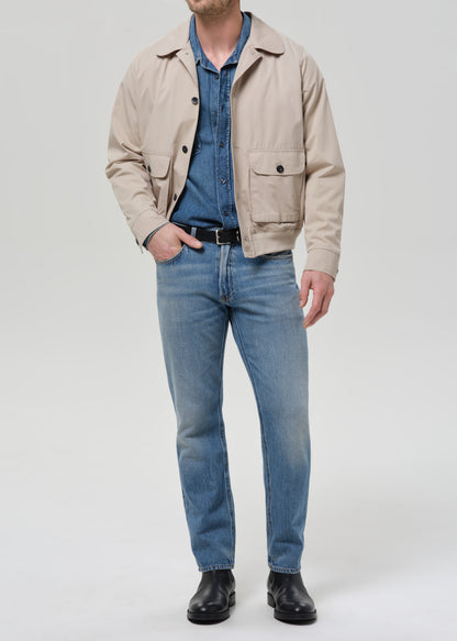 Person wearing a beige jacket, blue shirt, and jeans on a white background