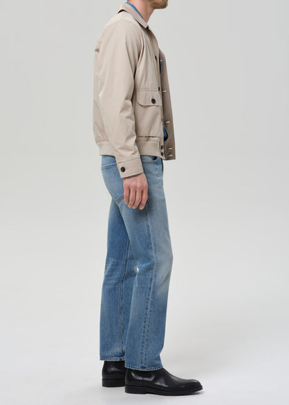 Person wearing a beige jacket and blue jeans on a plain background