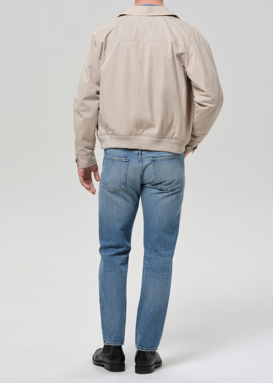 Person wearing a beige jacket and blue jeans on a white background