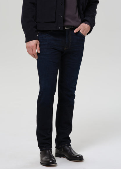 Person wearing dark indigo straight leg jeans with a black bomber jacket and dark charcoal crewneck tee on a grey background.