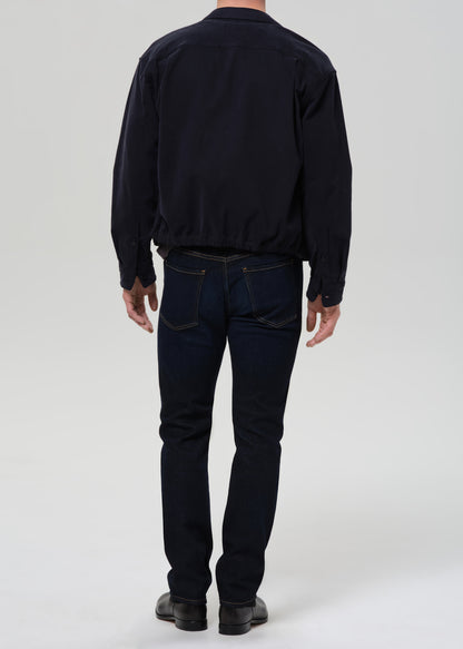 Person wearing dark indigo straight leg jeans with a black bomber jacket and dark charcoal crewneck tee viewed from the back on a grey background.