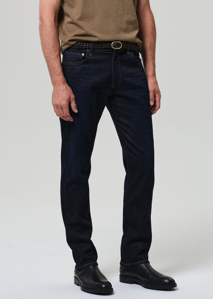 Person wearing dark blue jeans and black shoes on a plain background