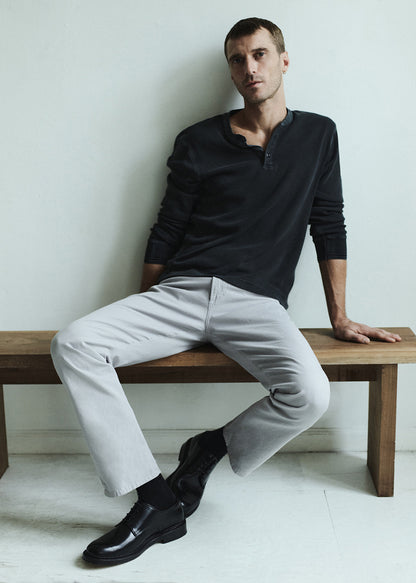 Man sitting on a wooden bench wearing a charcoal long-sleeve shirt, light gray pants, and black shoes.