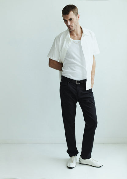 Man wearing a white shirt over a white-shirt with black pants on a plain background