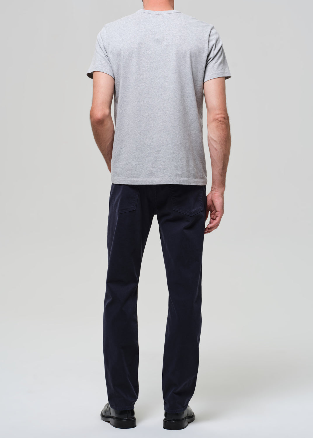 Person wearing a gray t-shirt and dark navy pants on a grey background