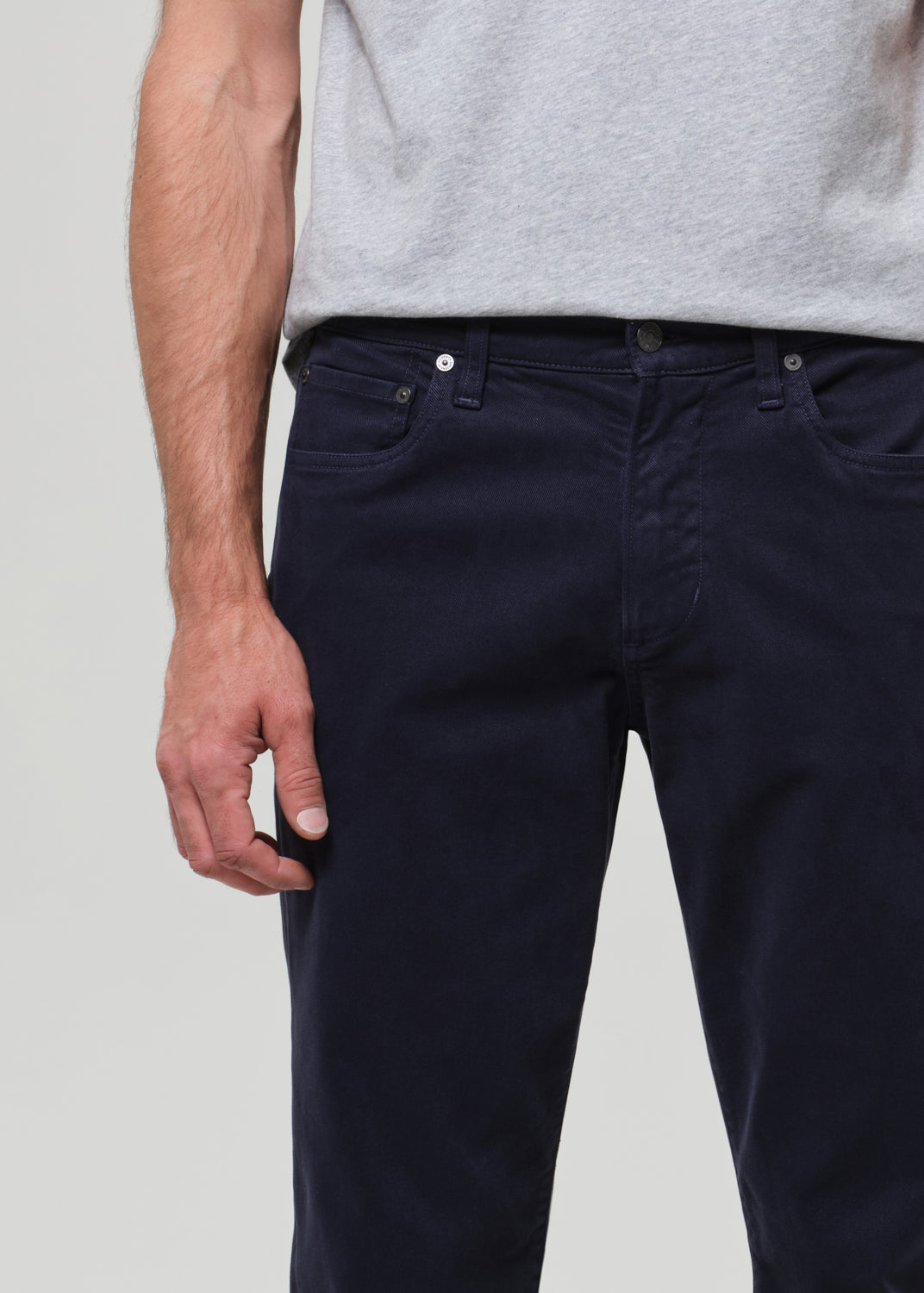 Person wearing a gray t-shirt and dark navy pants on a grey background