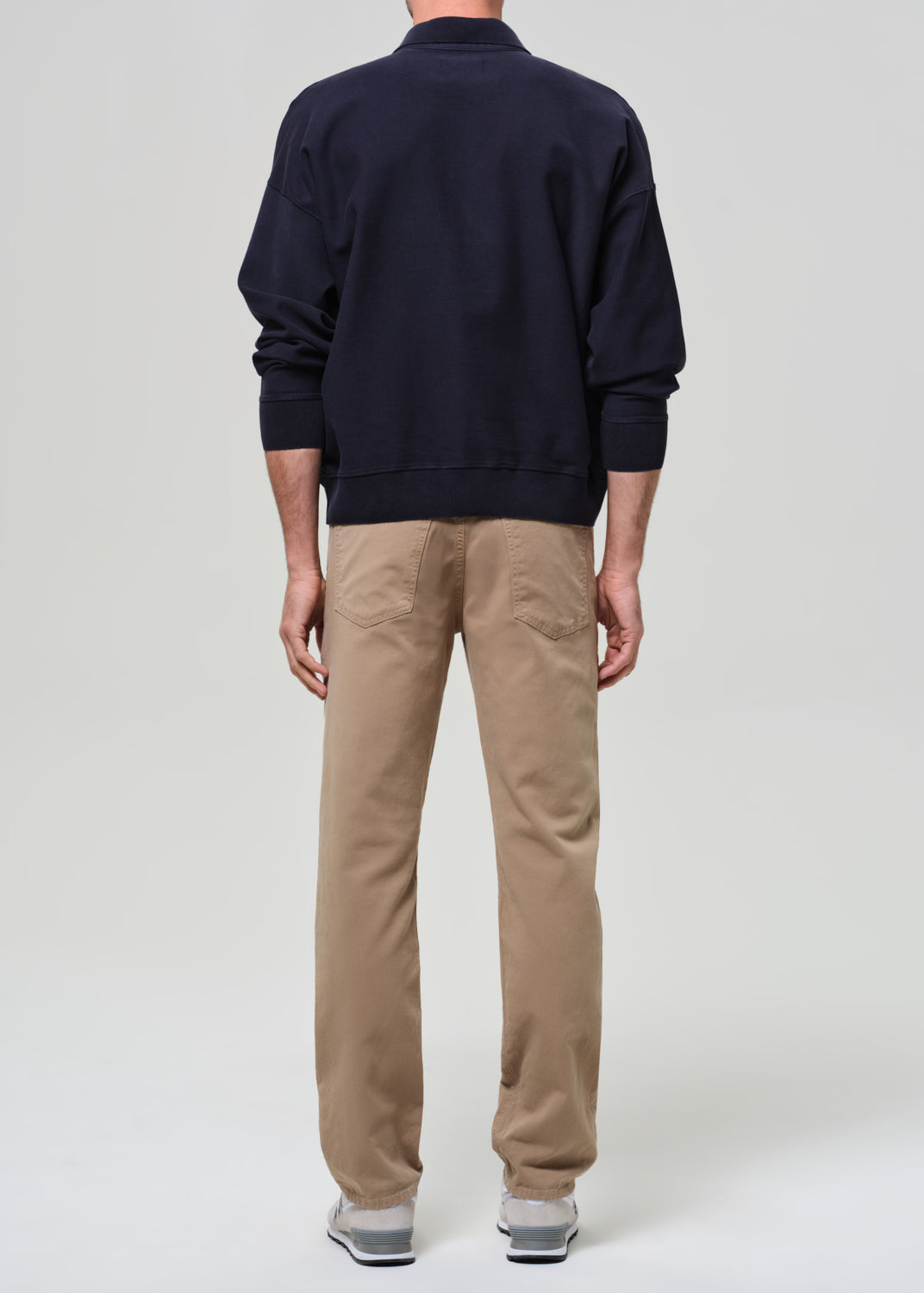 Person wearing a navy sweater and beige pants on a plain background