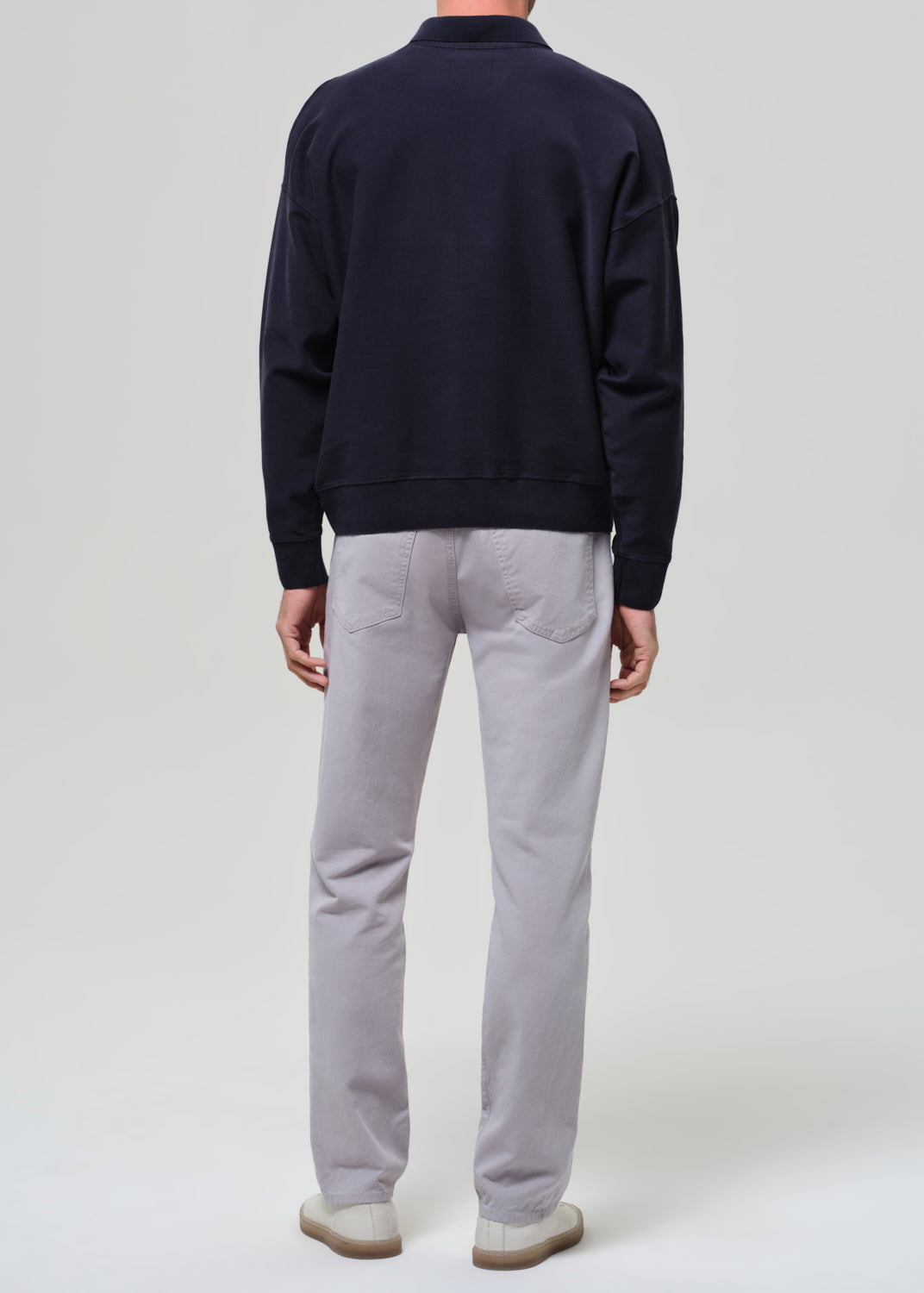 Person wearing a navy poly and light gray pants on a plain background
