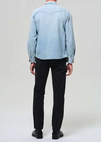 Person wearing a light blue denim shirt and black pants on a white background