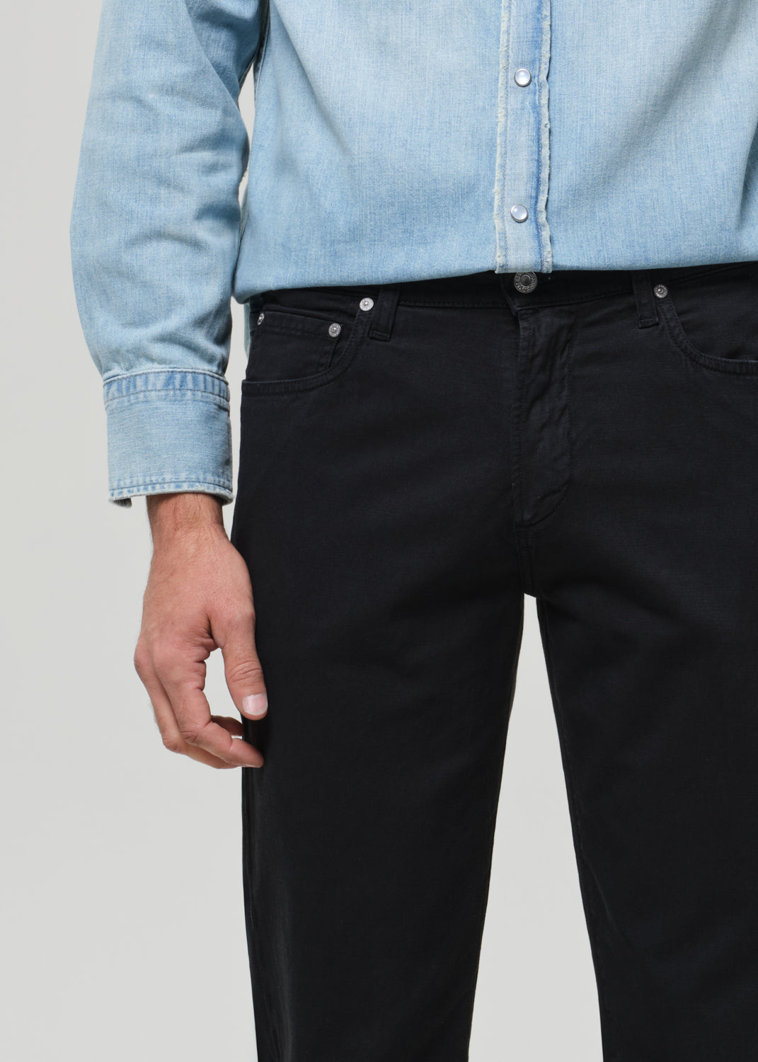 Person wearing a light blue denim shirt and black pants on a plain background