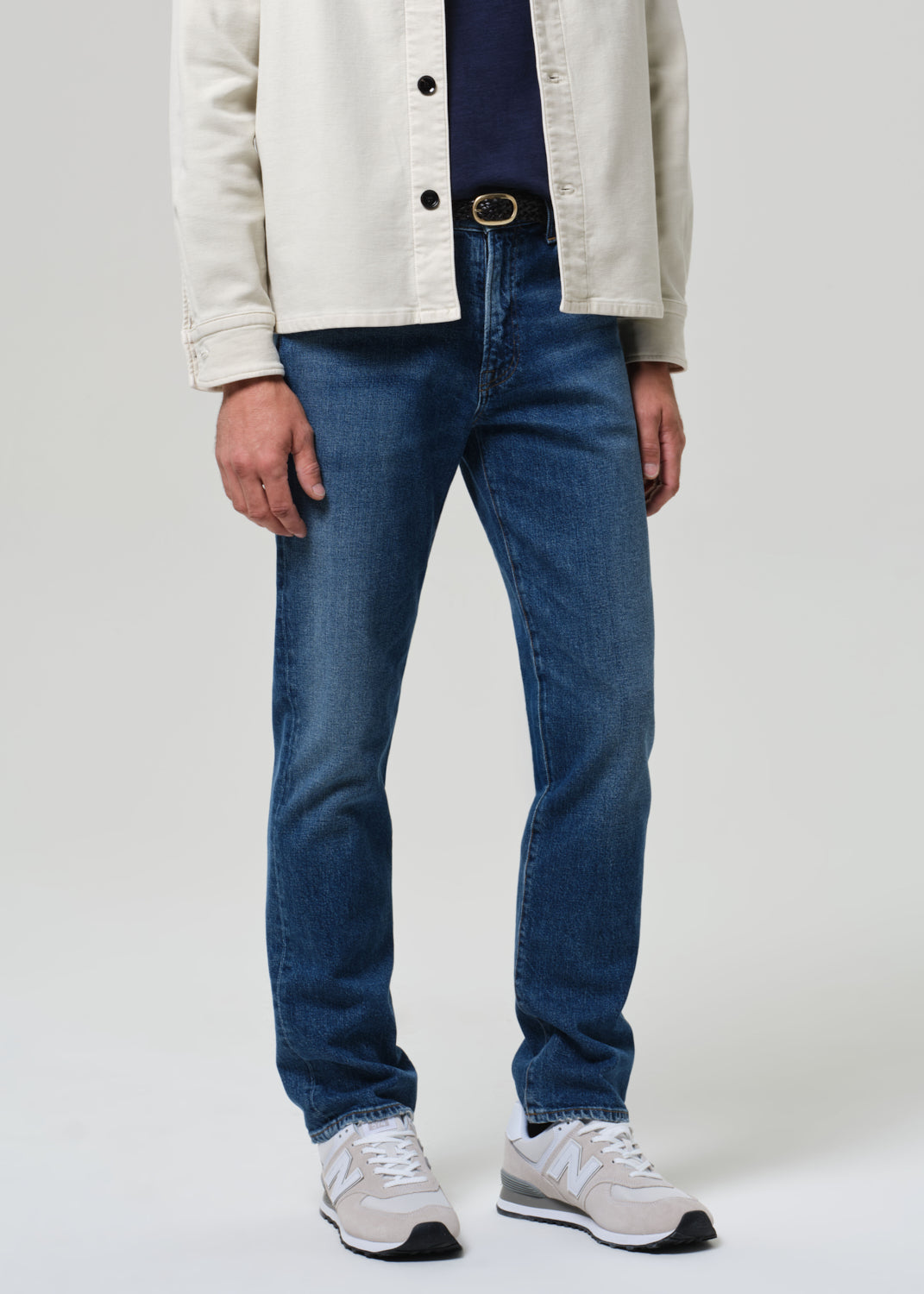 Person wearing blue jeans and a beige jacket on a plain background