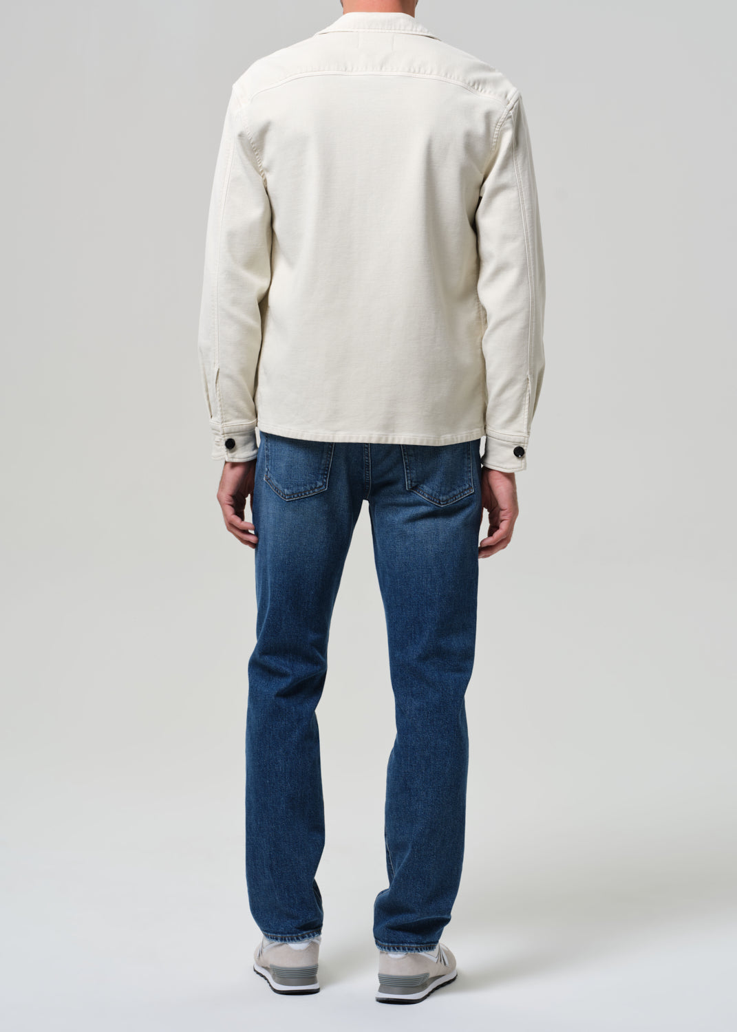 Person wearing a light-colored jacket and blue jeans on a plain background