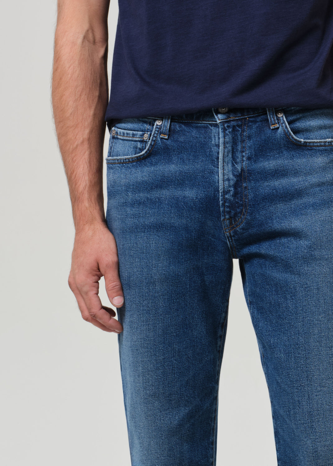 Person wearing blue jeans and a dark shirt on a light gray background