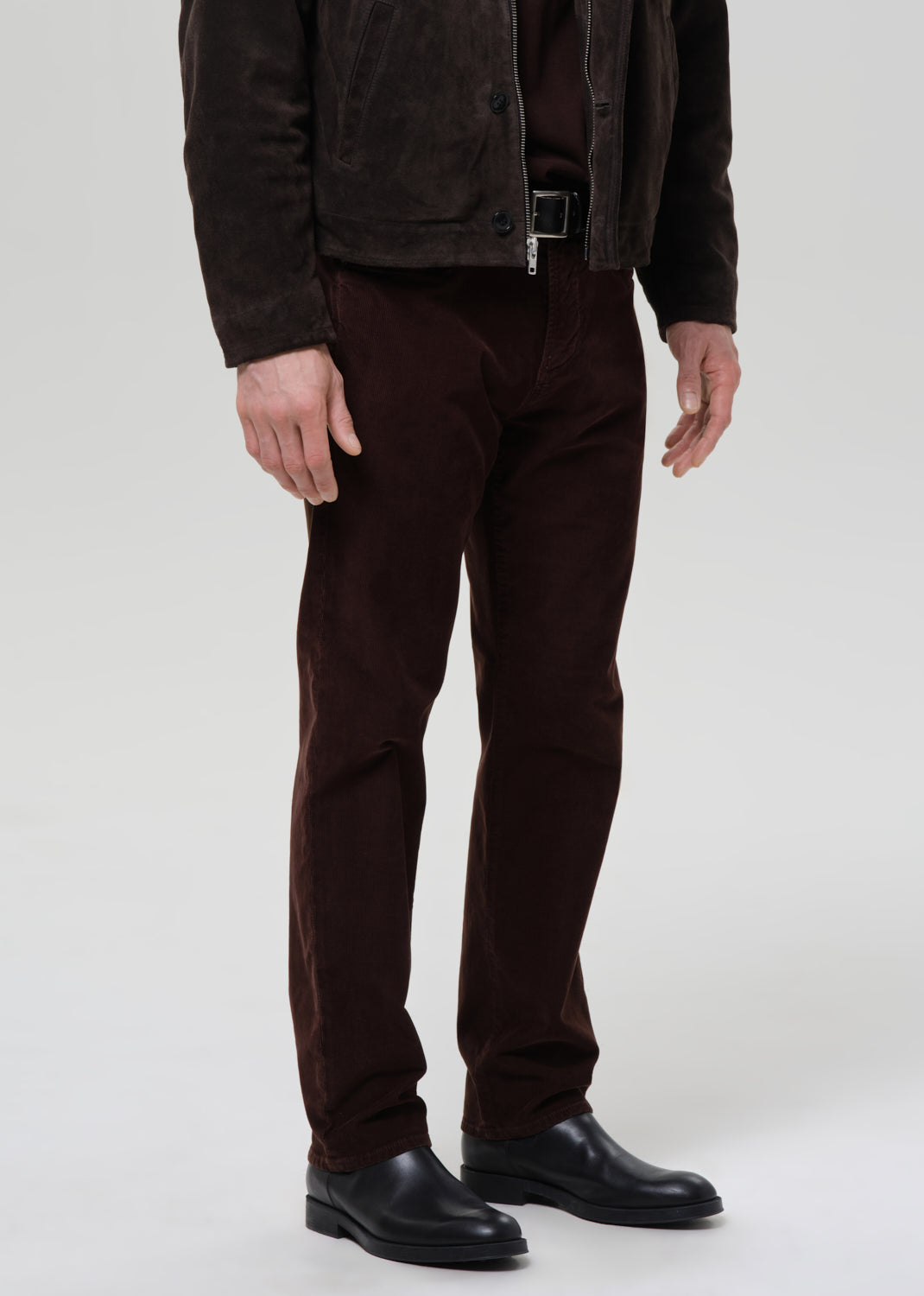 Person wearing a brown jacket, pants, and shoes on a grey background
