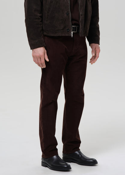 Person wearing a brown jacket, pants, and shoes on a grey background