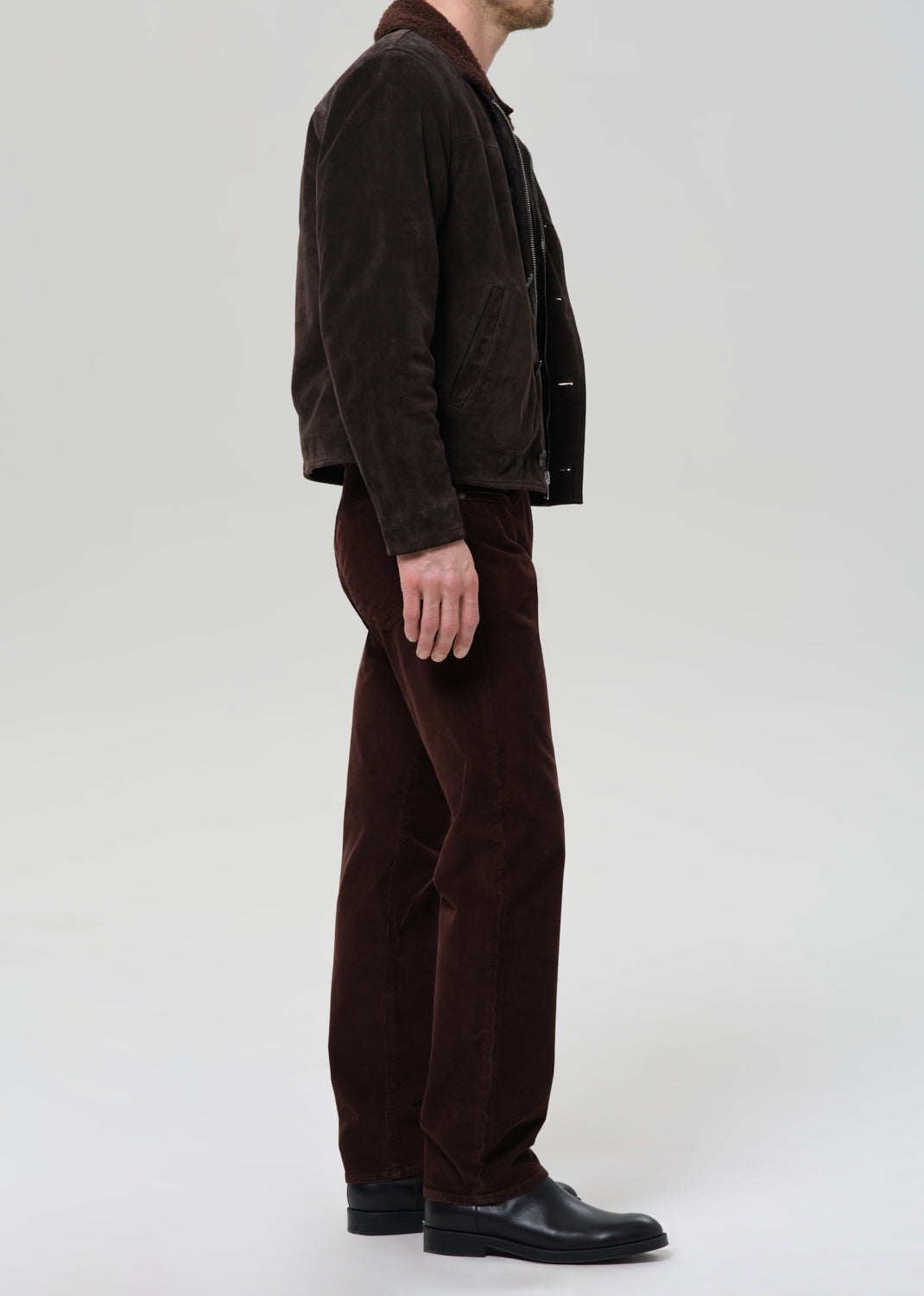 Person wearing a brown jacket and pants on a grey background