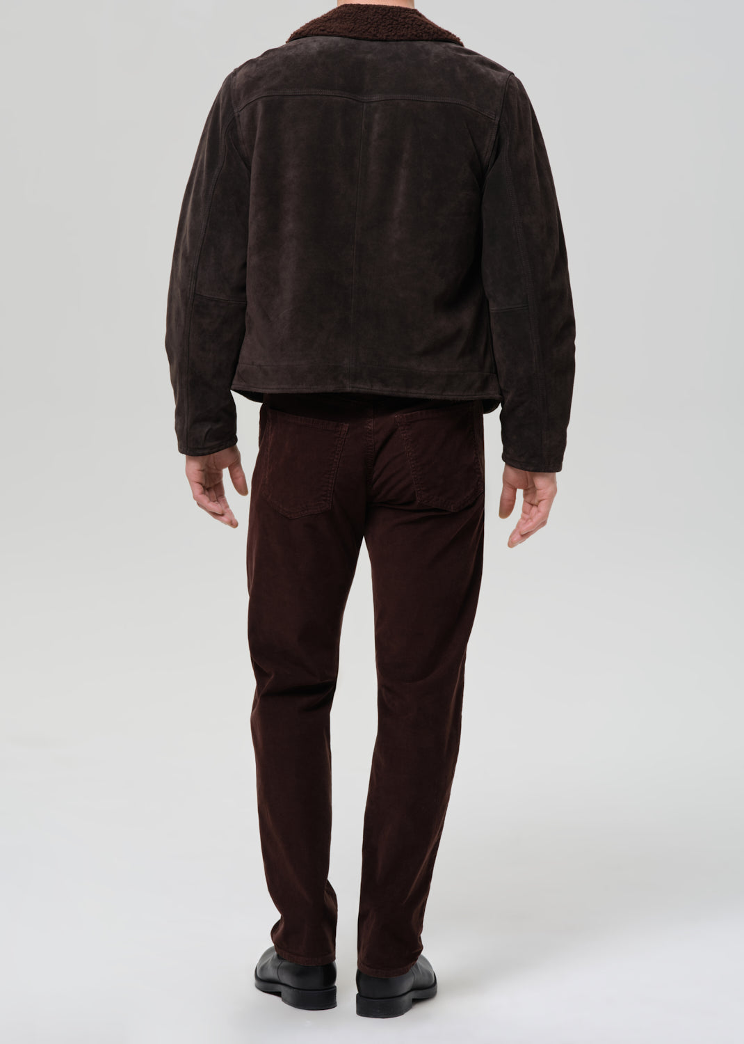 Person wearing a brown corduroy jacket and pants on a grey background