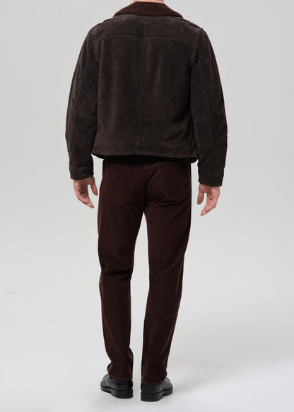 Person wearing a brown corduroy jacket and pants on a grey background