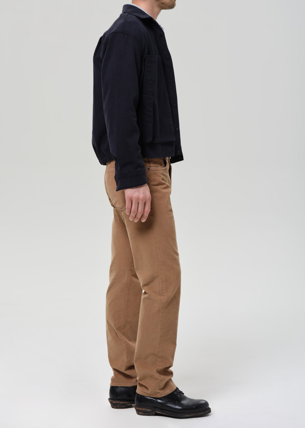 Person wearing a black jacket and brown pants on a grey background