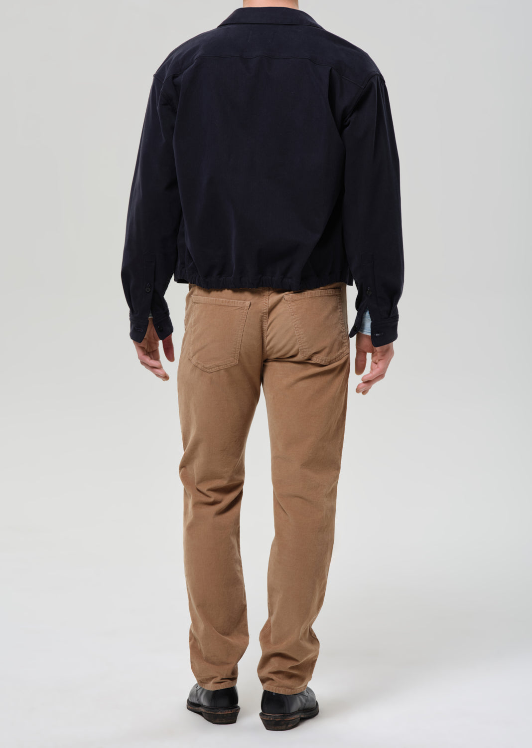 Person wearing a black jacket and tan pants on a grey background