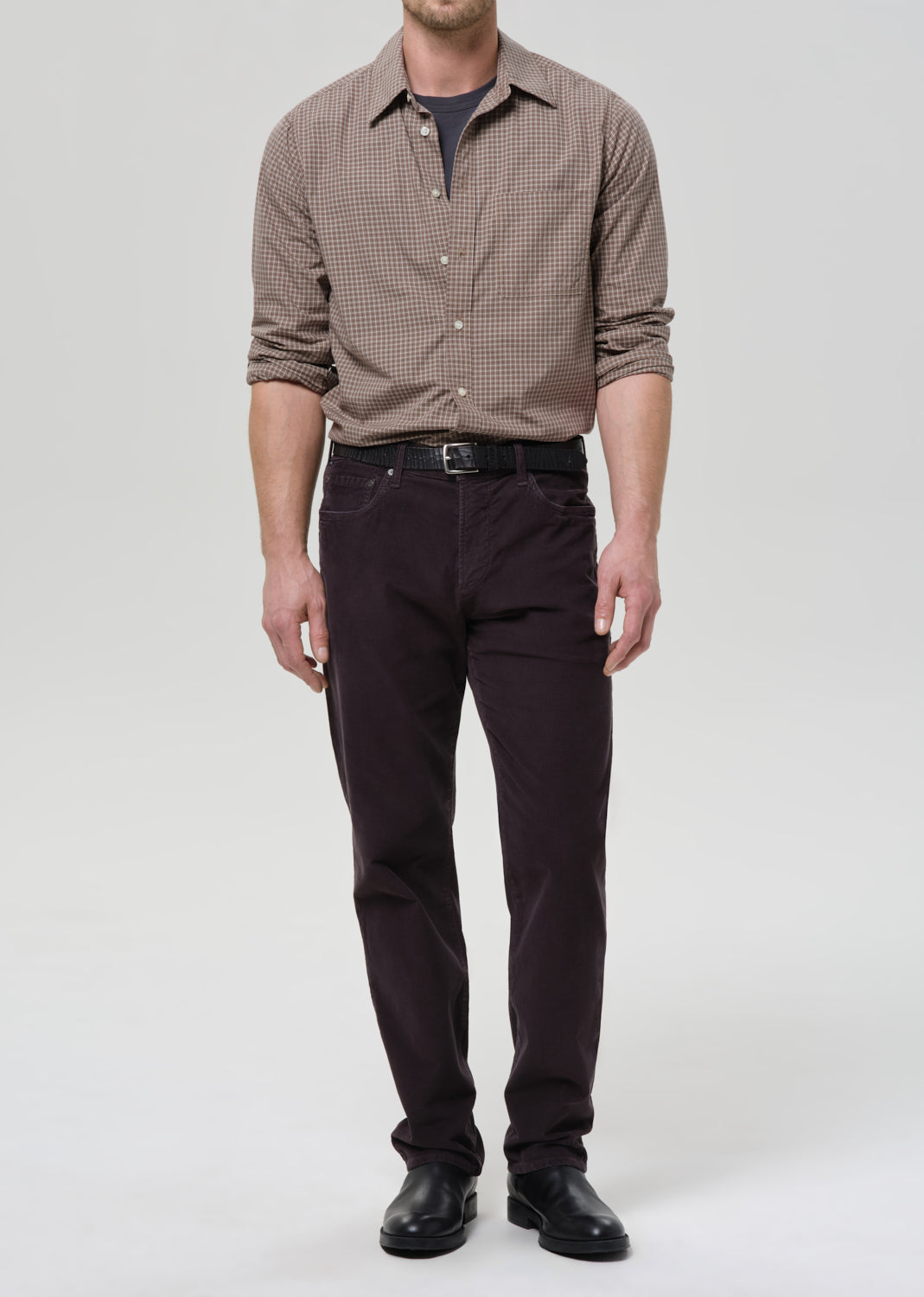 Man wearing a dark grey checkered shirt and dark pants on a grey background