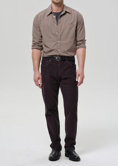 Man wearing a dark grey checkered shirt and dark pants on a grey background
