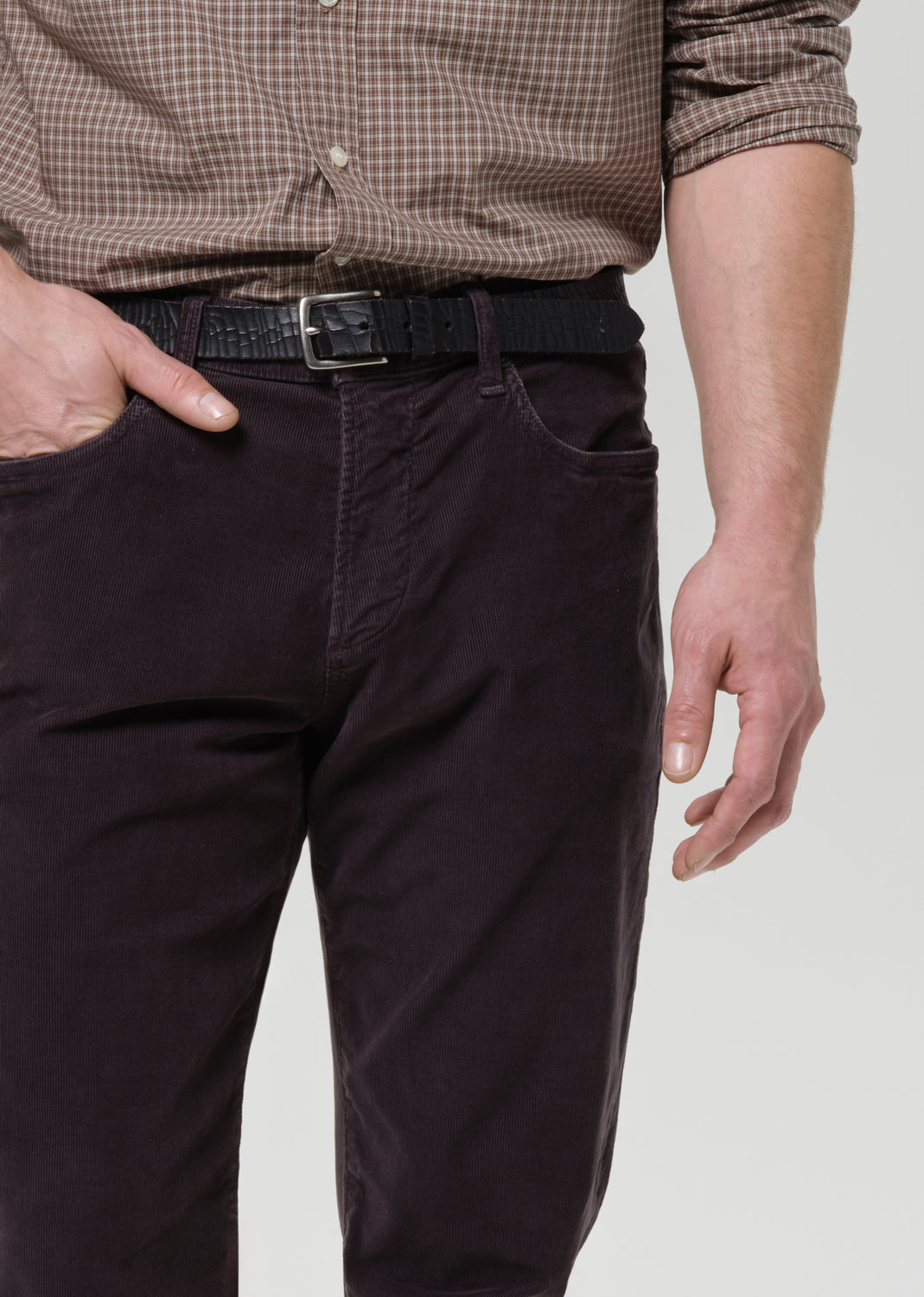 Person wearing a brown checkered shirt and dark grey pants on a grey background