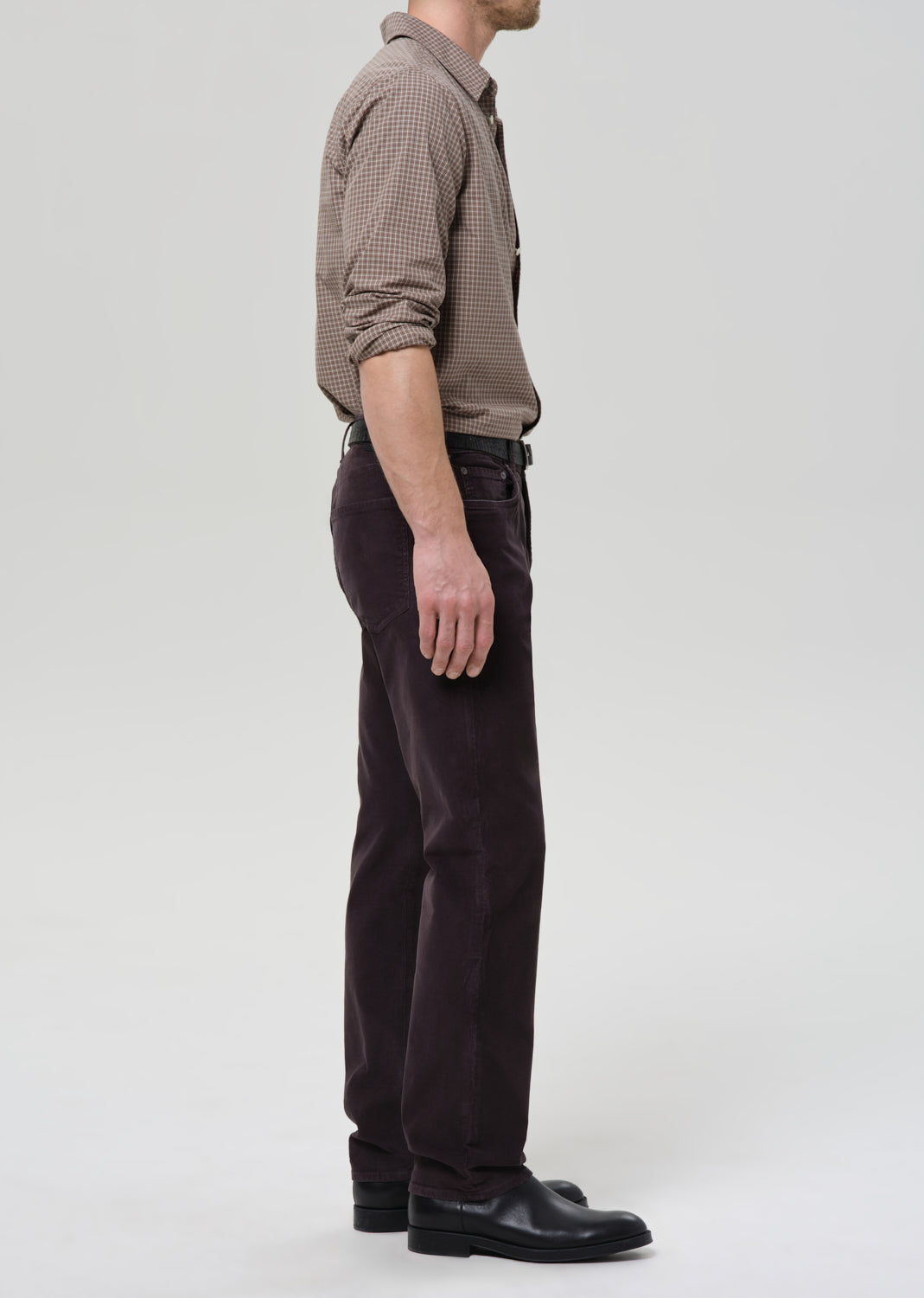 Person wearing a brown checkered shirt and dark grey pants on a grey background