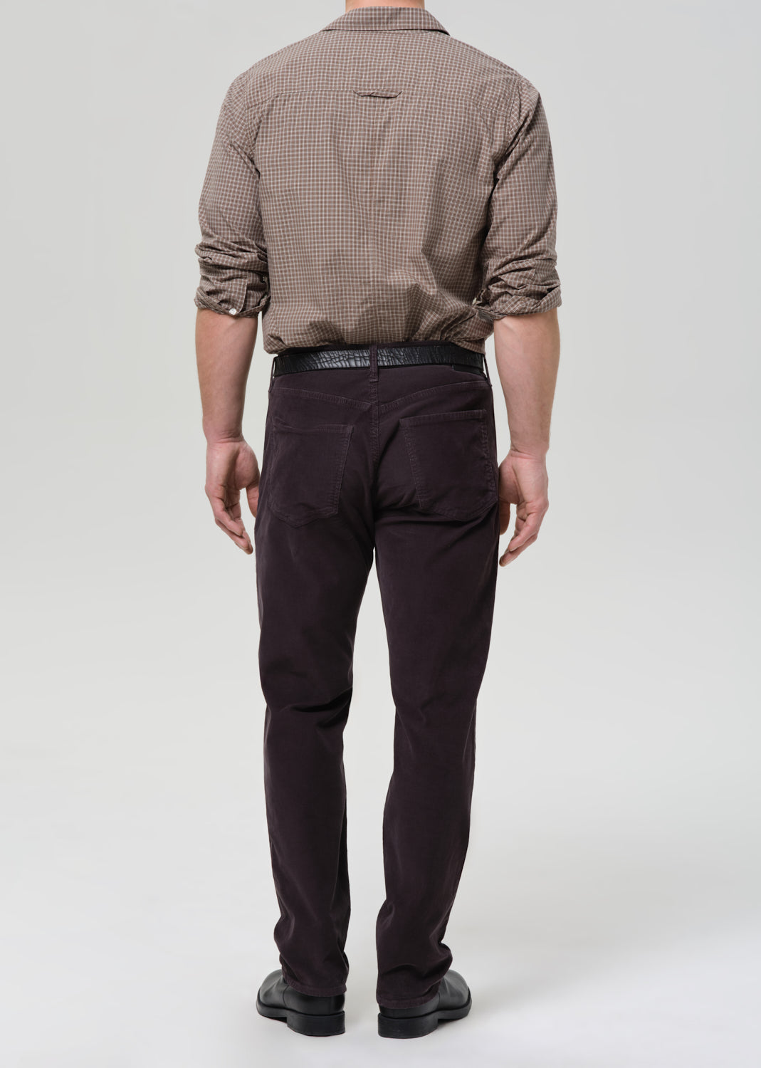 Person wearing a brown checkered shirt and dark grey pants on a grey background