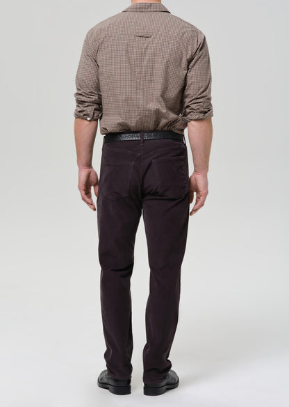 Person wearing a brown checkered shirt and dark grey pants on a grey background