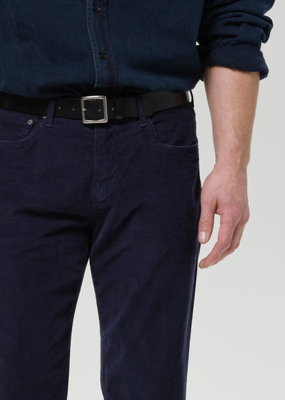 Person wearing navy blue pants and shirt with a belt on a grey background