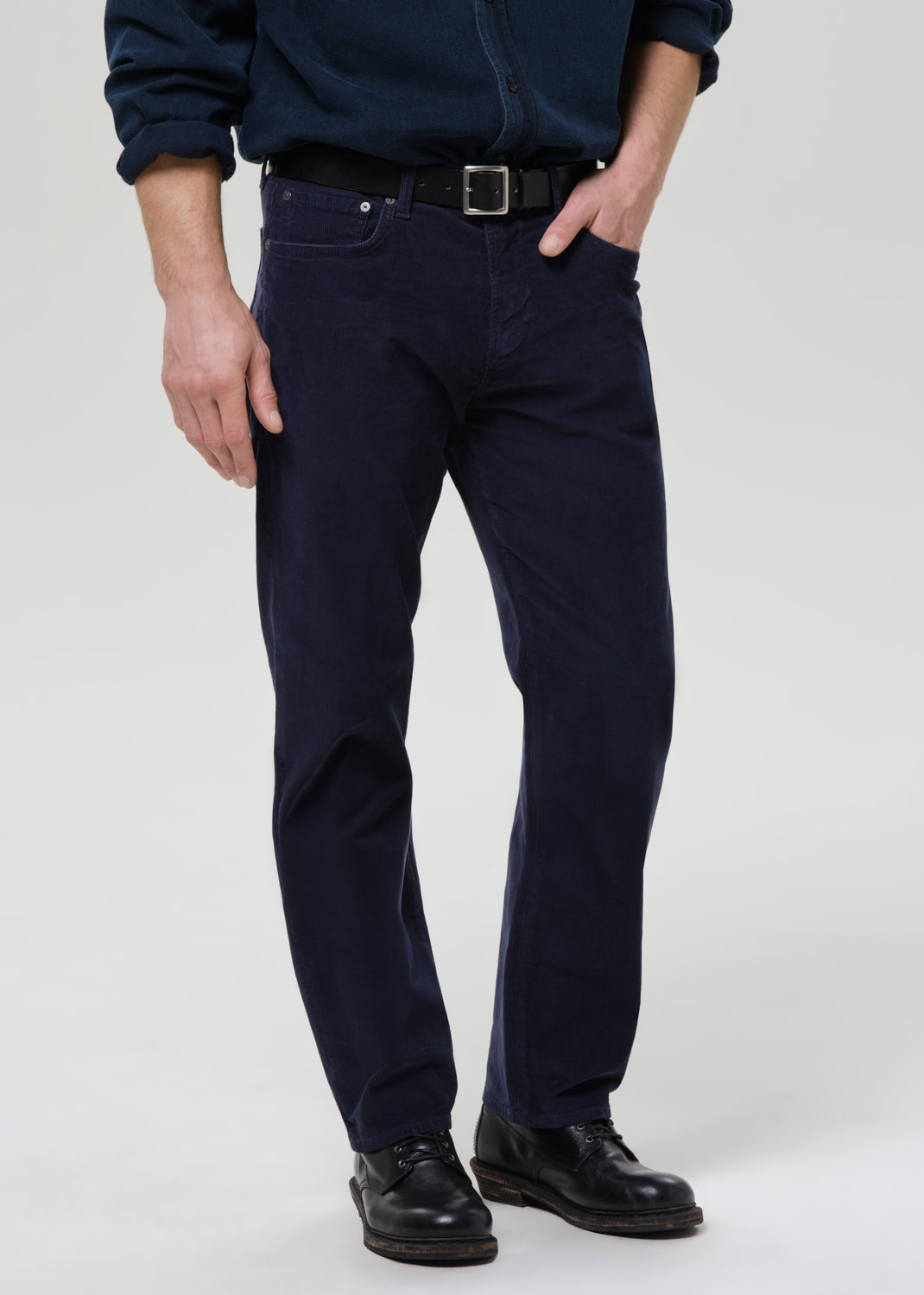 Person wearing navy blue pants and black shoes on a grey background