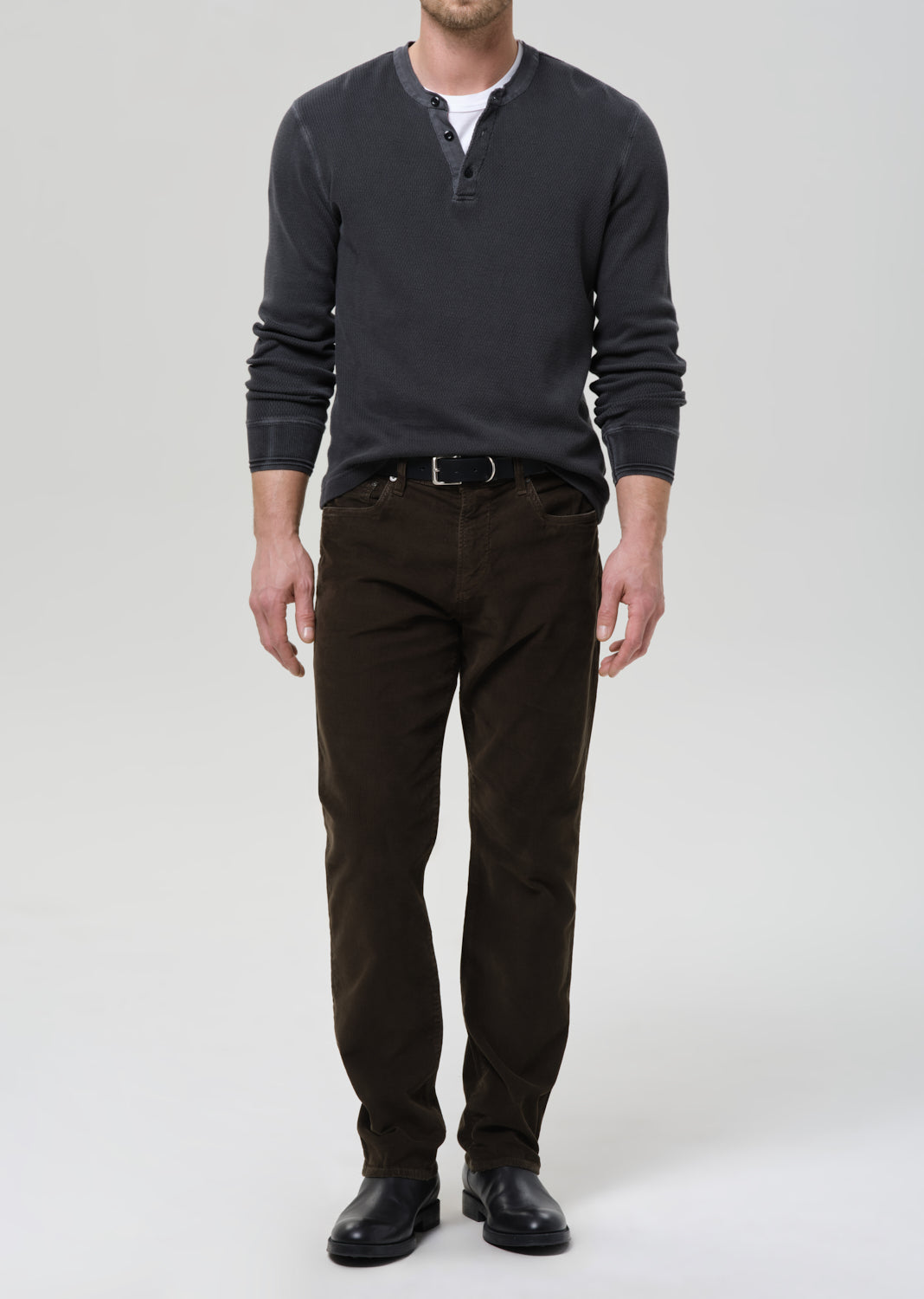 Man wearing a dark gray long-sleeve shirt and brown pants on a grey background