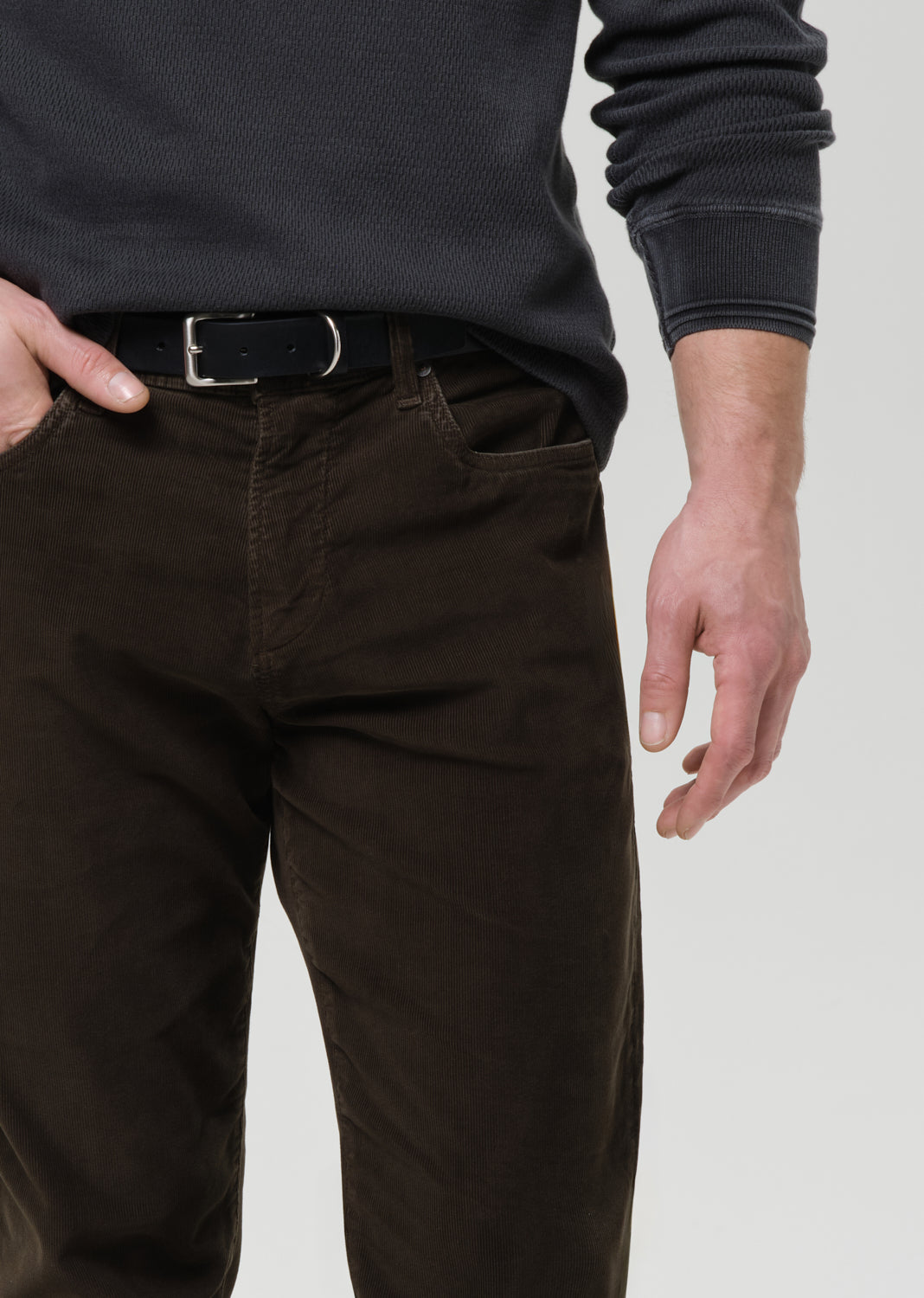 Person wearing dark brown pants and a black shirt on a grey background
