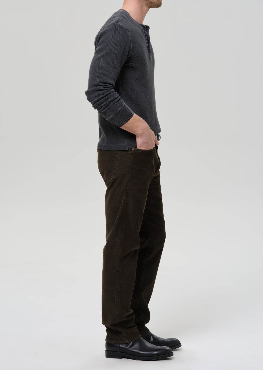 Person wearing a dark gray long-sleeve shirt and brown pants on a grey background