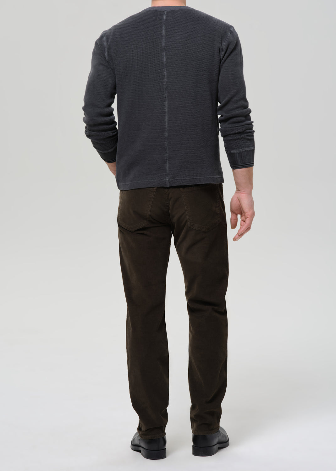 Person wearing a dark gray long-sleeve shirt and brown pants on a grey background
