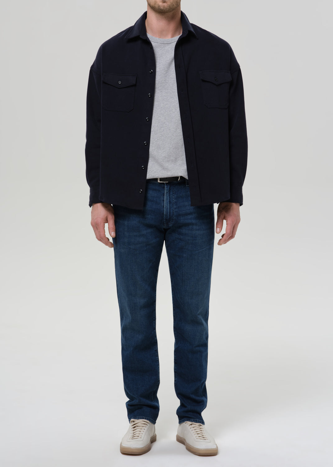 Person wearing medium blue straight leg jeans with a navy bomber jacket and light grey crewneck tee on a grey background.
