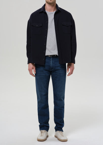 Person wearing medium blue straight leg jeans with a navy bomber jacket and light grey crewneck tee on a grey background.