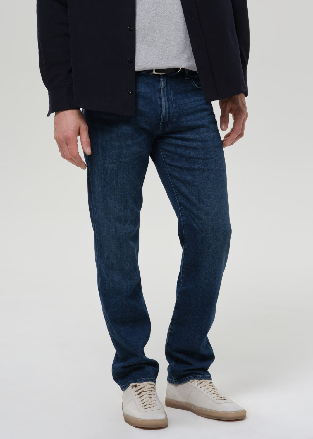 Person wearing medium blue straight leg jeans with a navy bomber jacket and light grey crewneck tee on a grey background.