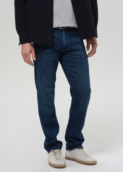 Person wearing medium blue straight leg jeans with a navy bomber jacket and light grey crewneck tee on a grey background.