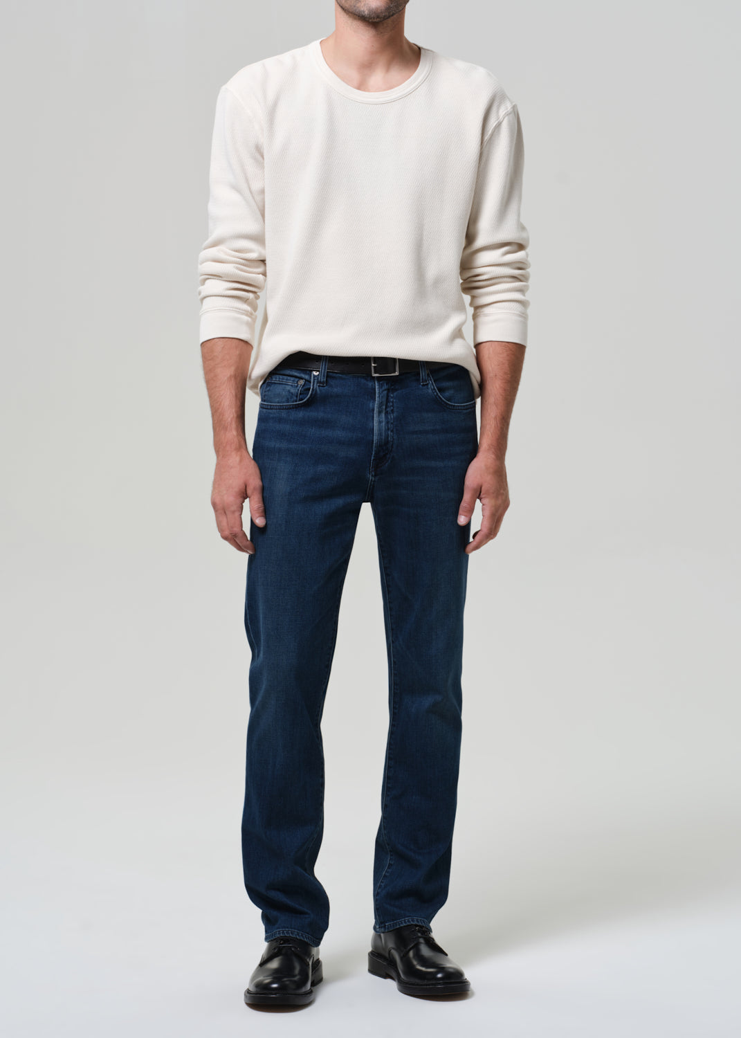 Person wearing a white sweater and blue jeans on a plain background