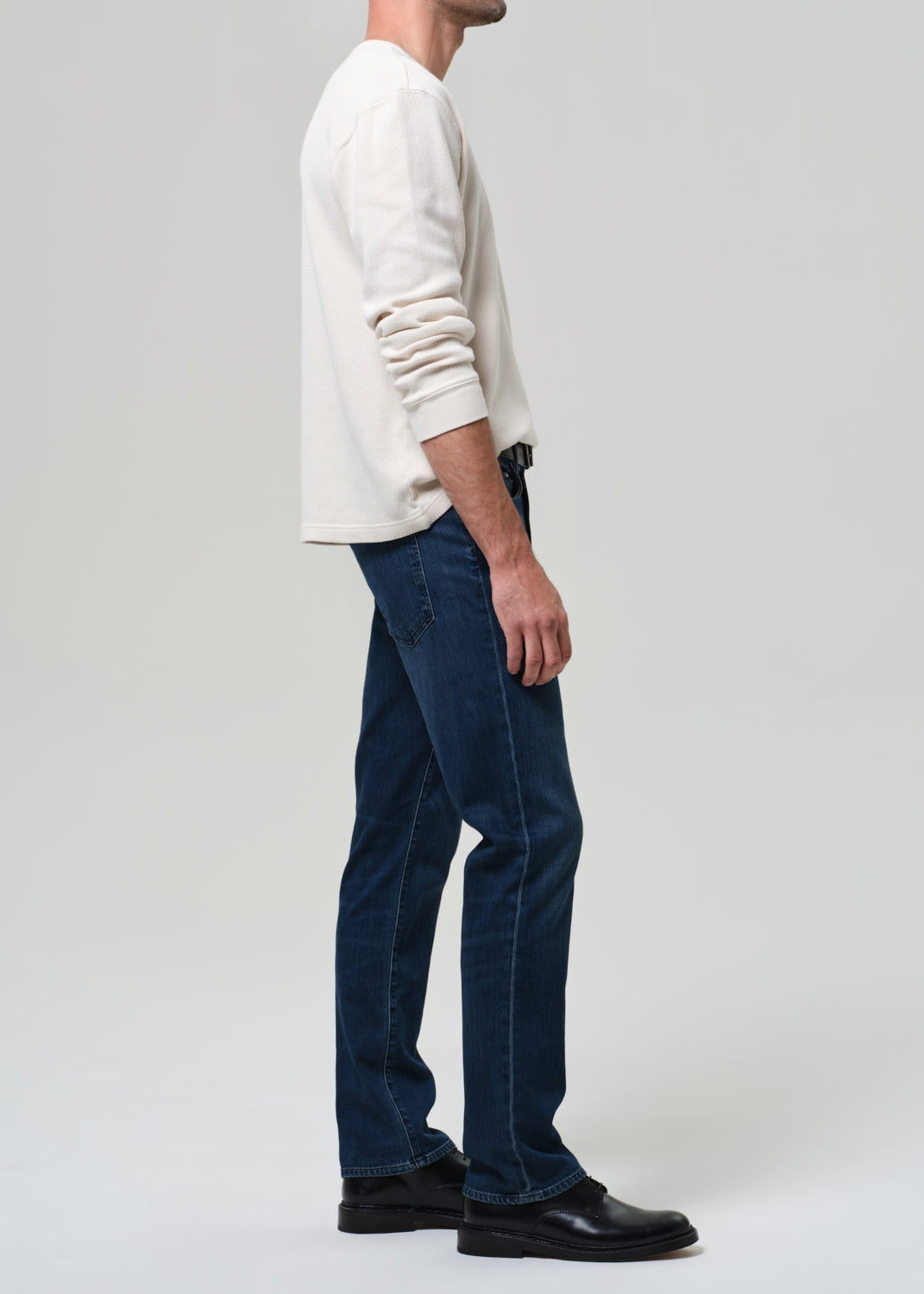 Person wearing a white sweater and blue jeans on a plain background