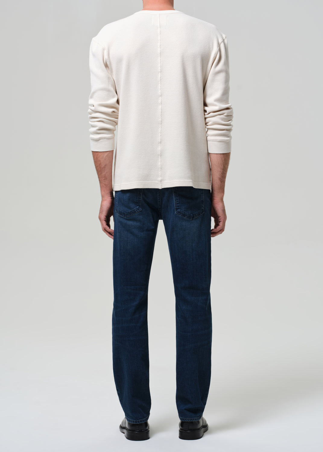 Person wearing a beige sweater and dark blue jeans on a plain background