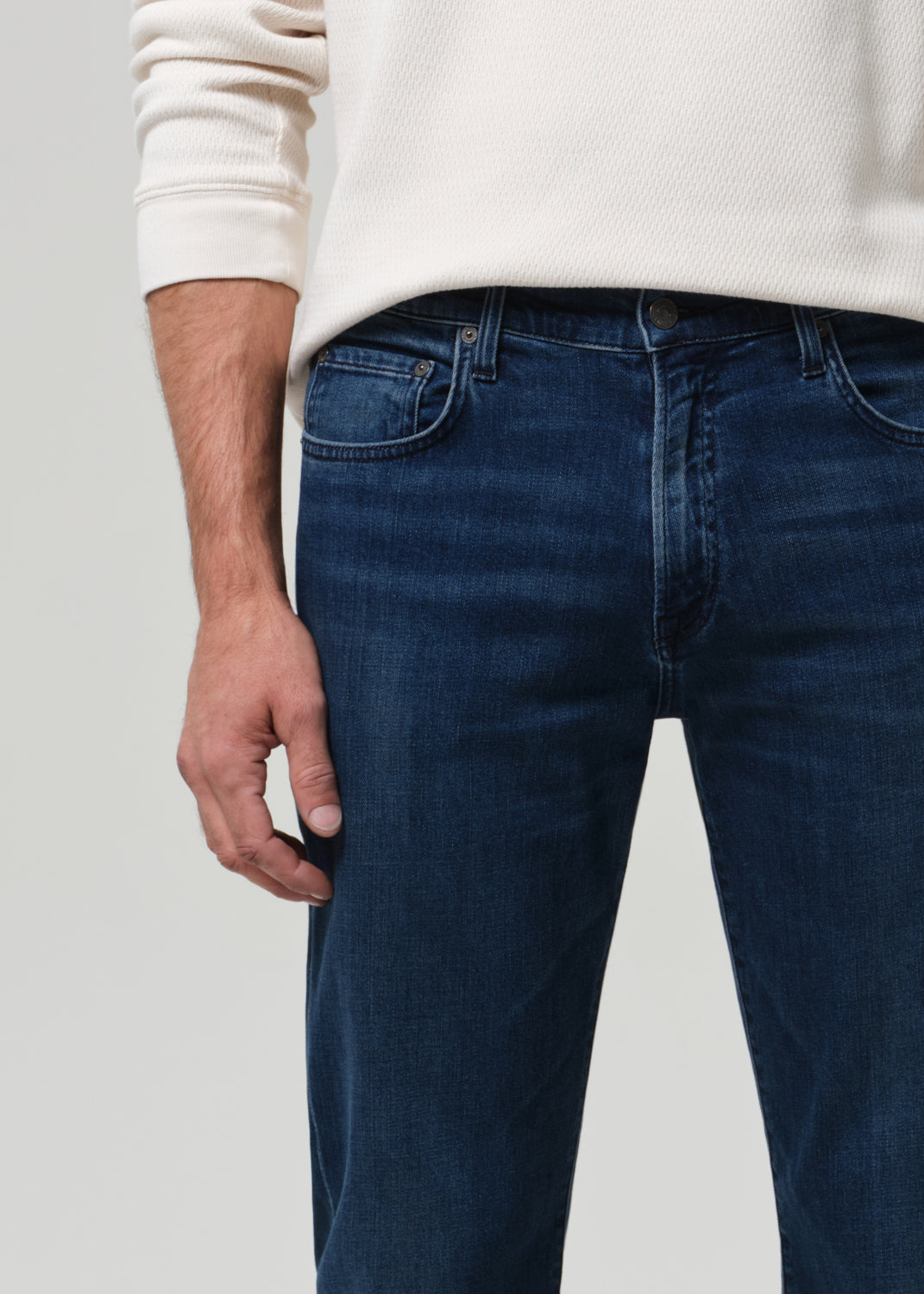 Person wearing blue jeans and a white sweater on a plain background