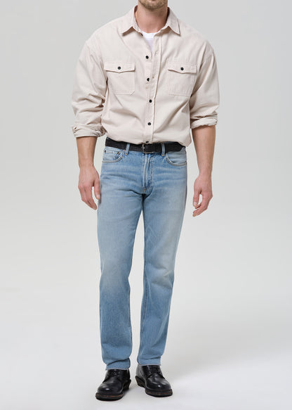 Man wearing a beige shirt, light blue jeans, and black shoes on a white background