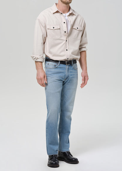 Person wearing a beige shirt, light blue jeans, and black shoes on a white background