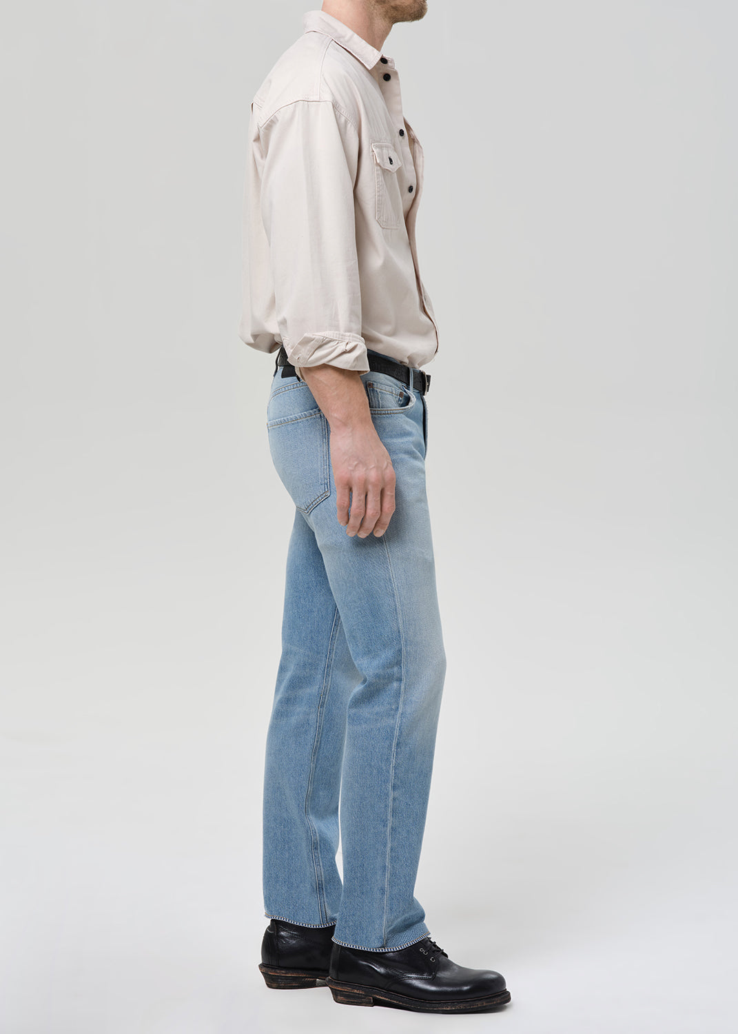 Person wearing a beige shirt and light blue jeans on a white background