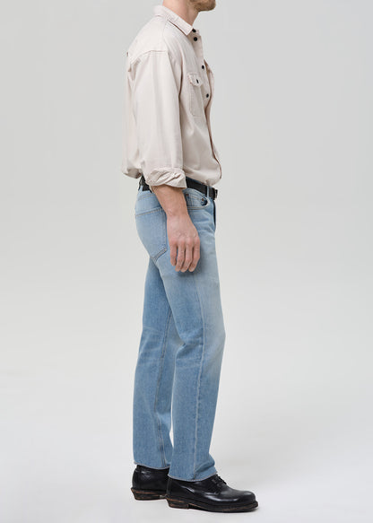 Person wearing a beige shirt and light blue jeans on a white background