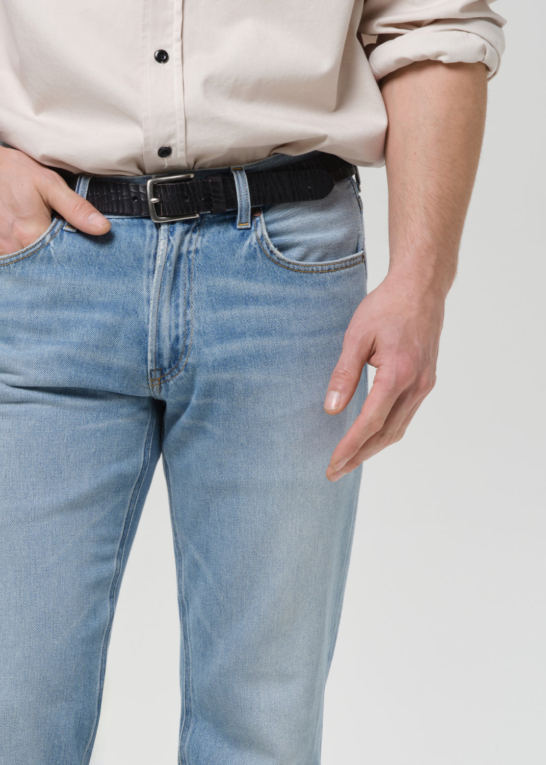 Person wearing a beige shirt and light blue jeans on a grey background